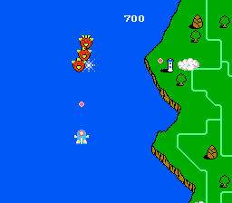 A side-scrolling shooter stage displays a yellow and orange bee sprite in the upper-left area of the screen, a white cloud formation in the center-left, and a score of 700 at the top. The right half shows a green vertical cliff or wall structure with black outlines and several small red enemy sprites positioned at different heights. The background is solid blue, representing sky, while the ground and terrain occupy the right portion with a stepped, blocky green landscape design typical of NES-era pixel art.