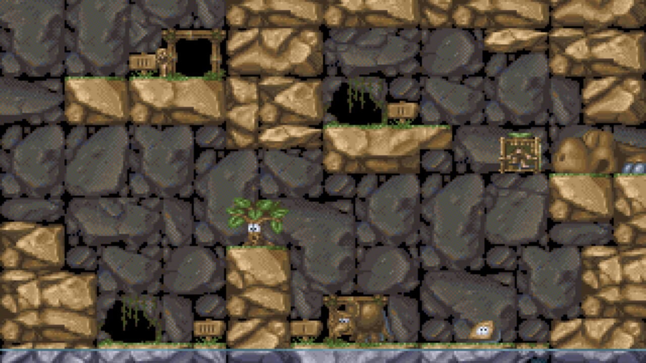 A side-scrolling platformer level displays a cavern made of gray and tan stone blocks with shadows. A small brown creature with a palm tree on its head stands on a tan platform in the center-left area. Additional creatures with similar appearance inhabit various platforms throughout the level. Vining green vegetation hangs from upper ledges. Small building structures and what appear to be treasure chests are scattered across different platforms. The bottom of the screen shows a blue-gray floor or boundary. The pixel art uses a limited color palette typical of early 1990s DOS games.