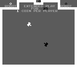 The title screen displays a gray background with menu text at the top reading "ROBOT," "EXTENDED PLAY," and "ROBOT" along with "1 COIN PER PLAYER" in white capital letters. Two small pixelated tank sprites appear in the center area—one white tank in the upper portion and one black tank positioned lower and to the right—against the plain gray play field.