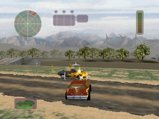 A brown vehicle drives across an arid desert landscape with an explosion detonating nearby. A radar circle and compass appear in the upper left, while a fuel or damage indicator displays vertically on the right side. Distant mountains and sparse palm trees frame a clear sky above the flat terrain. The vehicle-based combat game uses a third-person perspective with a visible minimap in the lower left corner.