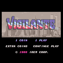 The Vigilante arcade title screen displays the game's logo in large red and blue pixelated letters centered over a cityscape background with tall buildings. Below the title are four menu options arranged horizontally: "1 COIN", "PLAY", "EXTRA COINS", and "CONTINUE PLAY". At the bottom, a copyright notice reads "© 1986 IREM CORP." in small white text. The overall color palette uses beige, gray, and blue tones typical of late-1980s arcade graphics.