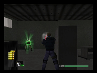 A player character in dark tactical gear stands in a dimly lit indoor environment facing a green glowing enemy figure. The character occupies the center-right of the frame with a weapon drawn. A green health bar appears at the bottom right of the screen. To the left, a yellow ammunition counter displays current inventory. The environment shows concrete walls, dark doorways, and recessed ceiling elements rendered in muted grays and blacks. The graphics display the characteristic low polygon count and limited texture detail typical of N64-era 3D rendering.