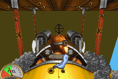 A first-person cockpit view displays an aircraft's control panel with two large mechanical gauges flanking a central instrument cluster. The windscreen shows a yellow aircraft nose in the foreground and a blue sky above. Red decorative elements and hanging ornaments frame the top edges of the cockpit. The art style uses pre-rendered 3D graphics with a warm color palette dominated by browns, oranges, and metallic grays. This appears to be a GBA port with reduced resolution compared to the original 1990 release.