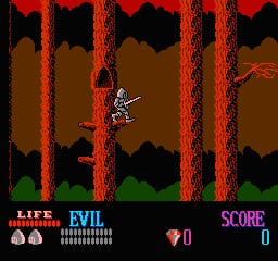 A knight character stands centrally in a brown cavern environment surrounded by tall red vertical pillars with black silhouettes of jagged rock formations between them. Green grass appears at the bottom of the screen. The HUD displays life hearts on the left, an evil meter in the center-left, a 0 score in purple text on the right, and a small red gem or potion icon in the upper right. The sprite uses white and brown pixel art against the dark brown background.