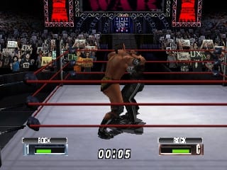Two wrestlers grapple in the center of a wrestling ring with white canvas and red ropes. The arena features a dark background with large red vertical banners and arena lighting visible above. Health bars labeled 'MAX' appear in the top left and right corners, with a timer showing '0:00:05' in the center. Crowd figures are visible in the stadium seating surrounding the ring. The graphics display the characteristic low-polygon 3D modeling and color palette typical of Nintendo 64 wrestling games.