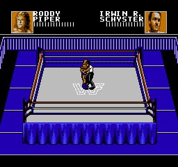 A wrestler stands in the center of a white wrestling ring surrounded by a blue steel cage with vertical bars. The ring is elevated on a blue platform with decorative railings. The background is solid blue. At the top of the screen, a scoreboard displays "RODDY" on the left and "LEARN P." on the right, each with health bars represented by vertical orange segments. The image uses 8-bit NES-style sprite graphics with a limited color palette of blue, white, orange, and black.