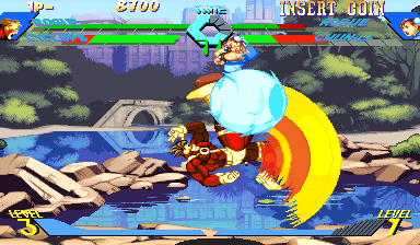 A 2D fighting game screenshot featuring two characters mid-combat in a water-based stage. The left character in red executes a spinning kick attack surrounded by yellow circular energy effects, while the right character in blue prepares a counterattack. The background shows a rocky shoreline with purple cliffs, brown wooden debris, and green bushes rendered in parallax layers. The HUD displays health bars at the top in green and red, character portraits in the upper corners, round timer showing "2/100," and a combo counter at the bottom left. The sprite animation depicts the arcade's characteristic 1996 hand-drawn aesthetic with vibrant colors and detailed backgrounds.