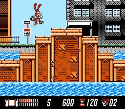 The Noid character jumps on wooden crates stacked in the water, with tall brown fortress-like structures on either side. A single red enemy or obstacle is visible in the upper left. The HUD displays health (1 unit), score (8), coins (600), timer (120), and lives (2) at the bottom. The background shows a light blue sky with brown buildings, water in blue, and pixel art rendered in the NES color palette with brown wooden textures dominating the level geometry.