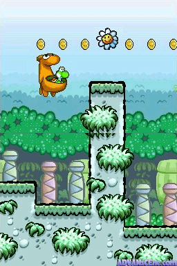 An orange Yoshi holds a green baby while positioned on a white pillar with grass tufts in the center of a pastel blue-green forest landscape. Multiple gold coins appear in a row across the top of the screen. The terrain below features layered green vegetation, gray stone platforms, and repeating grass clumps in the lower portion. The background shows a hazy forest silhouette with parallax depth. The sprite-based graphics use a colorful palette typical of Game Boy Advance-era graphics.