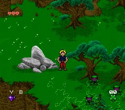 A young wizard character stands in a green forest environment surrounded by brown trees and gray rocks. White sparkles scatter across the grass. The bottom-left corner displays a purple inventory icon with 'Y B' text labels. The bottom-right shows additional UI elements including what appear to be action buttons. The sprite-based graphics use a 16-bit color palette typical of SNES-era games, with brown, green, and gray tones dominating the scene.
