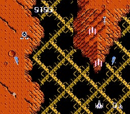 A top-down scrolling shooter displays a player spacecraft positioned in the lower-center area, firing at enemies arranged across a geometric grid of black and yellow diamond patterns. The background is predominantly orange with scattered small projectiles and debris. Enemies appear as white and red pixelated sprites distributed across the playfield. A score indicator reading "916" appears in the upper-left corner. The visual style uses low-resolution sprites typical of 8-bit NES graphics with a limited color palette of orange, black, yellow, white, and red.