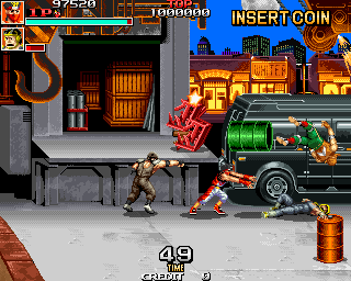 A male soldier character stands in the center of an urban street facing a green military truck with a mounted gun on the right side. Behind the truck, a warehouse with orange-lit doors and wooden crates occupies the left background. A score display at the top shows 97520 points and 100000 for the second player, with an "INSERT COIN" prompt. The bottom displays "49" and "CREDIT 1" in white text. The sprite-based graphics use a dark color palette with warm accent colors for the building and vehicle details.