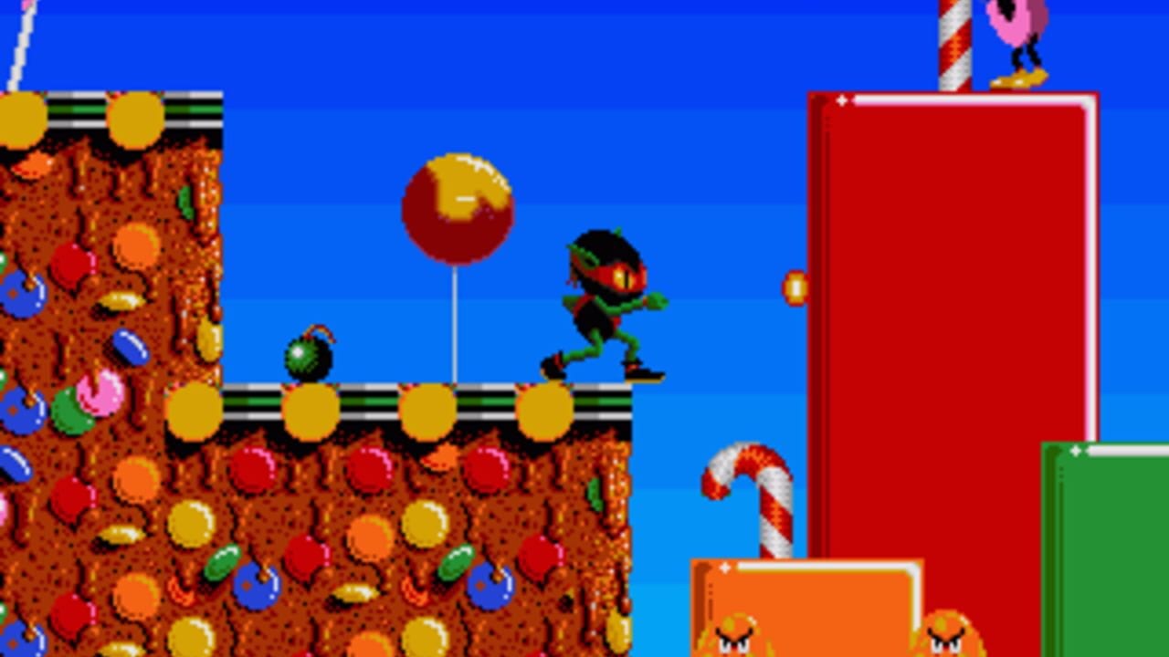 A green ninja character runs across a yellow platform suspended over brown rocky terrain filled with colorful gems and spheres in a bright blue sky. A large red ball on a pole floats in the center background, while red and green rectangular structures stand to the right. The left side shows a yellow vehicle or machine above the gem-covered ground. Candy cane and character sprites appear in the upper corners against the blue background. The scene uses 16-bit pixel art with distinct color contrast between the blue sky, brown earth, and platform elements.