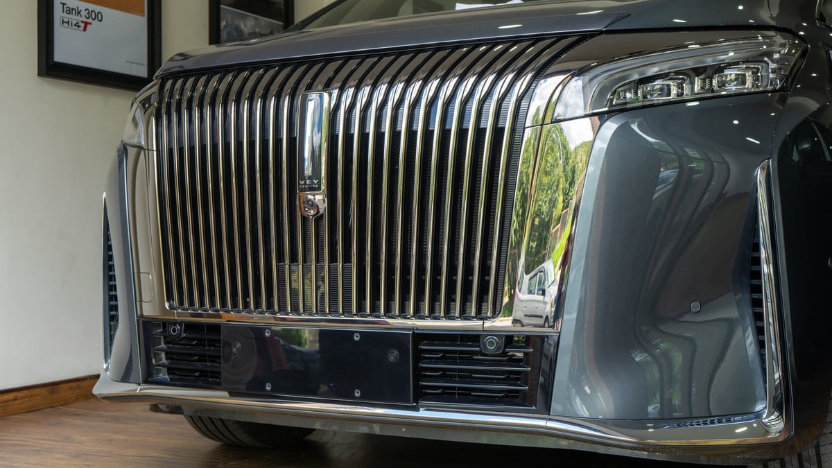 The WEY G9 grille in close-up, a framed Tank 300 Hi4-T print on the wall behind