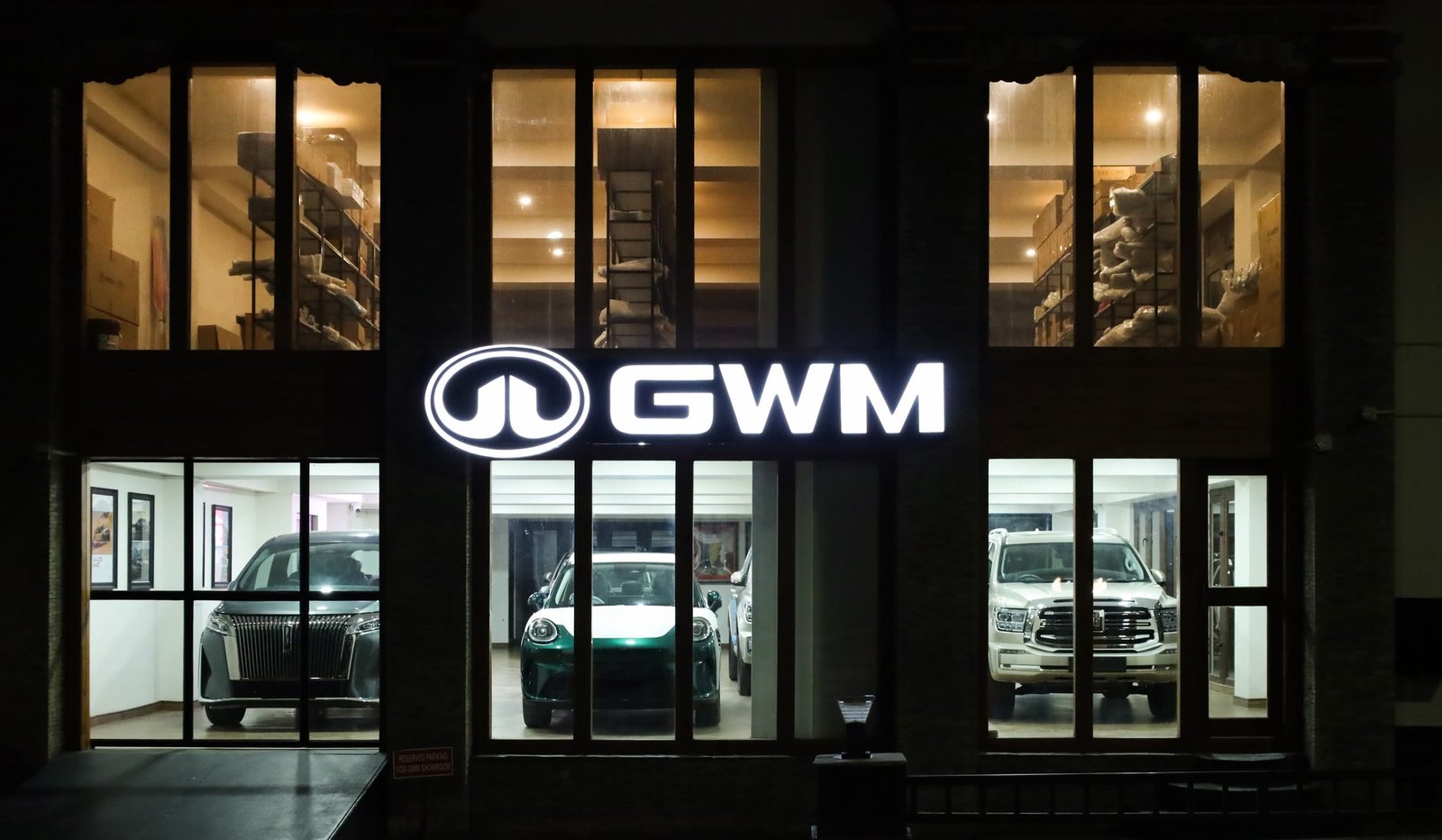 The illuminated GWM sign above the glass showroom entrance at night