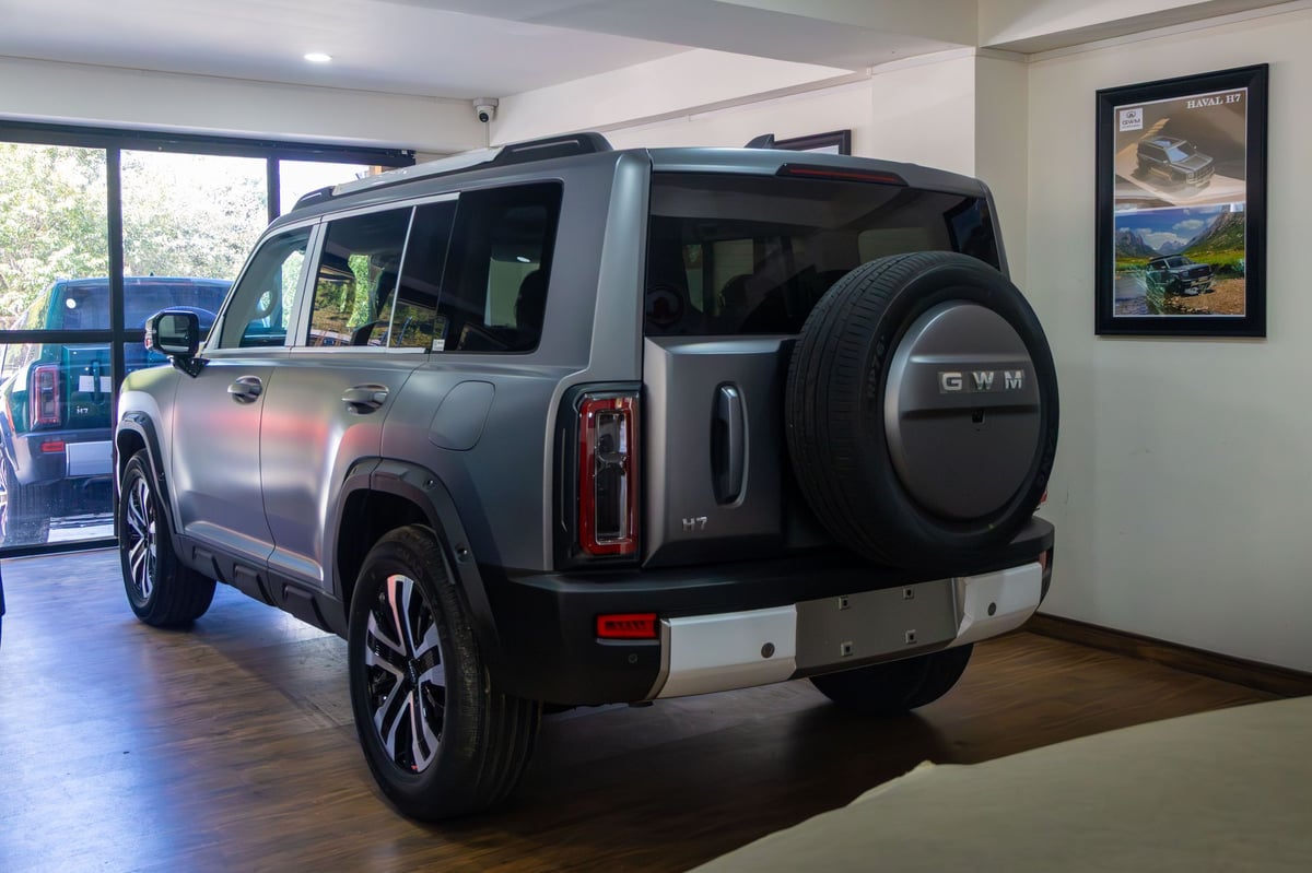 Matte-grey Haval H7 from the rear three-quarter inside the showroom, spare wheel on the tailgate