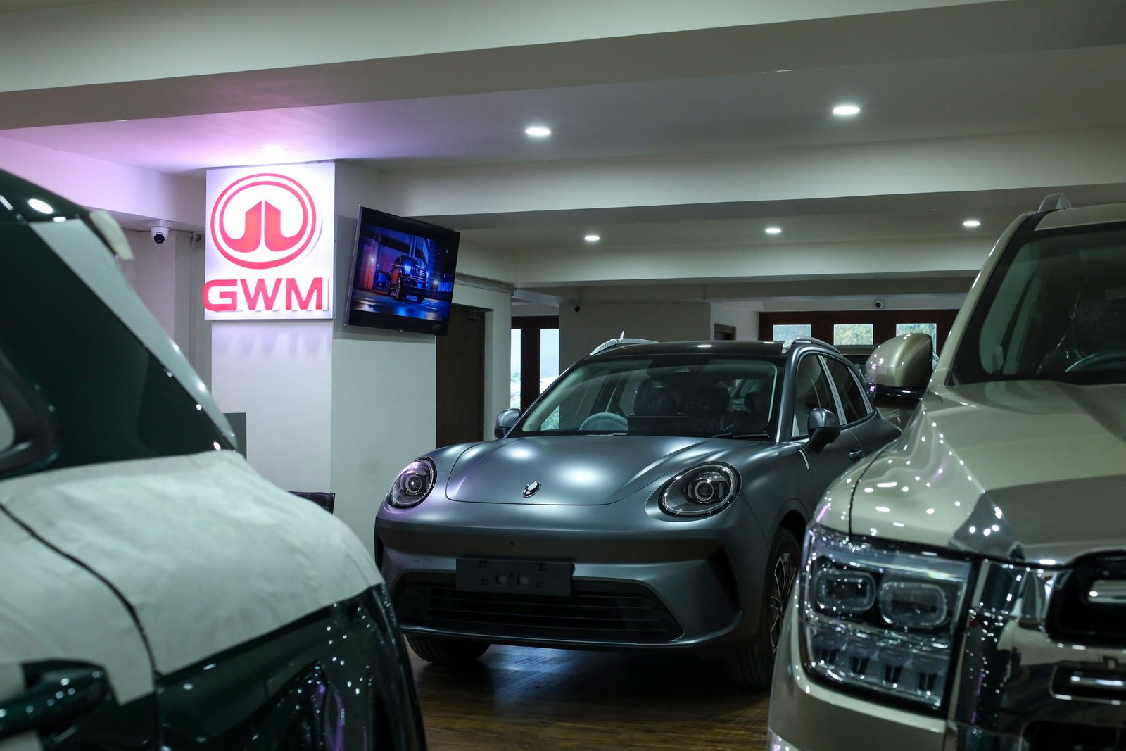 Silver ORA 5 head-on beneath the lit GWM pillar, flanked by two SUVs