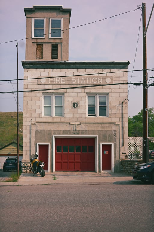 Coleman's former fire station with a pale stone facade, red garage door and narrow tower.