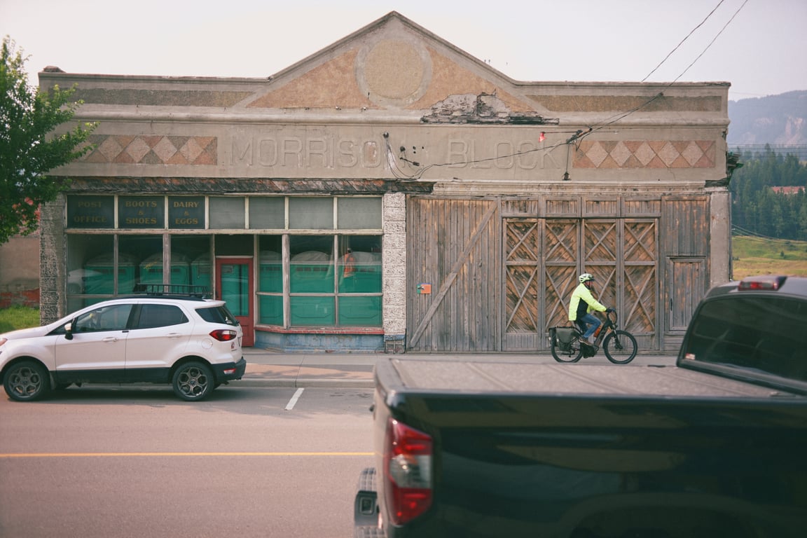 A cyclist rides past the worn Morrison Block storefronts with mountains behind Coleman.
