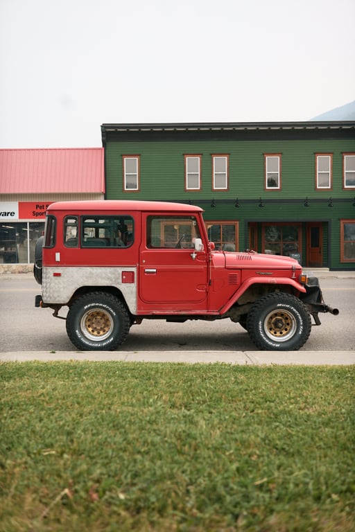 A red vintage Toyota Land Cruiser parked across from a green commercial building in Coleman.