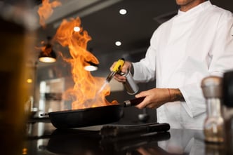 A chef is cooking in the kitchen of a restaurant, seen from the side