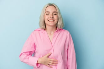 A young Caucasian woman gently touches her tummy while smiling softly, despite experiencing a slight discomfort in her upper abdomen