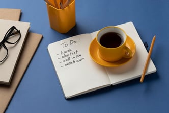 A notebook with a to-do list sits on a desk next to a cup of coffee