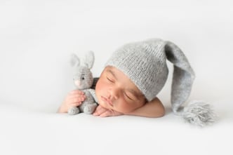 Adorable newborn peacefully sleeping in a grey crocheted hat, snuggled up with a toy rabbit