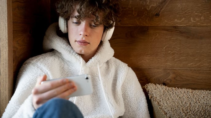 Gen Z teenager sitting on his bed, listening to music on his smartphone