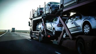 A car transport trailer filled with numerous vehicles travels along a highway