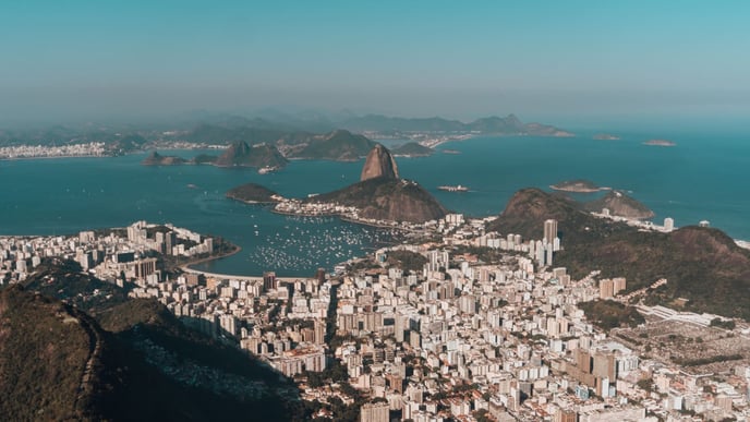 Aerial view of Rio de Janeiro, nestled between lush hills and the ocean, all beneath a clear blue sky