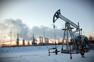 An oil pump stands against an industrial landscape, set against a winter sky filled with smoke