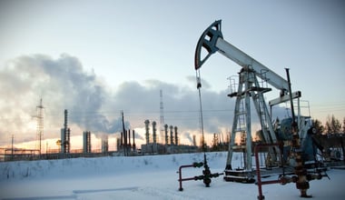 An oil pump stands against an industrial landscape, set against a winter sky filled with smoke