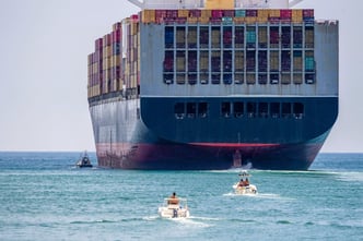 Container ship close to shore, accompanied by a tugboat and smaller vessels