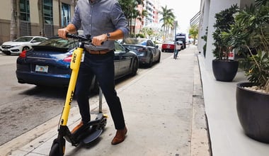 Modern executive man using Bolt, dockless electric scooter, in the streets of Brickell (Miami) with a Porsche behind him