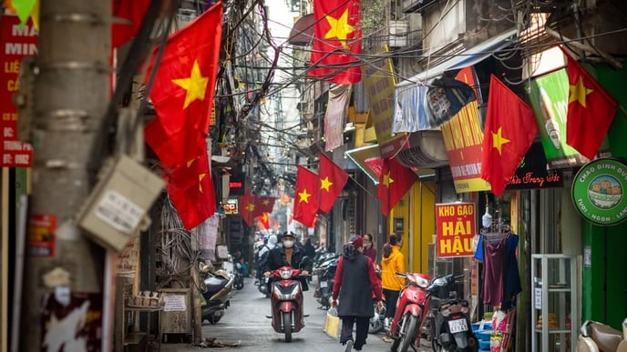 People go about daily life under Vietnamese flags in a narrow residential alleyway called Kham Thien Market in Hanoi, Vietnam