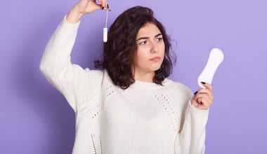 Thoughtful dark-haired woman contemplating the choice between tampons and sanitary napkins