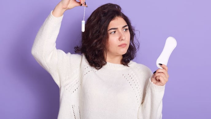 Thoughtful dark-haired woman contemplating the choice between tampons and sanitary napkins