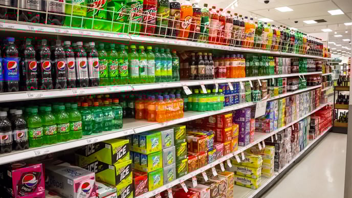 A view of the soda aisle of a grocery store, featuring several brands and colors of carbonated beverages