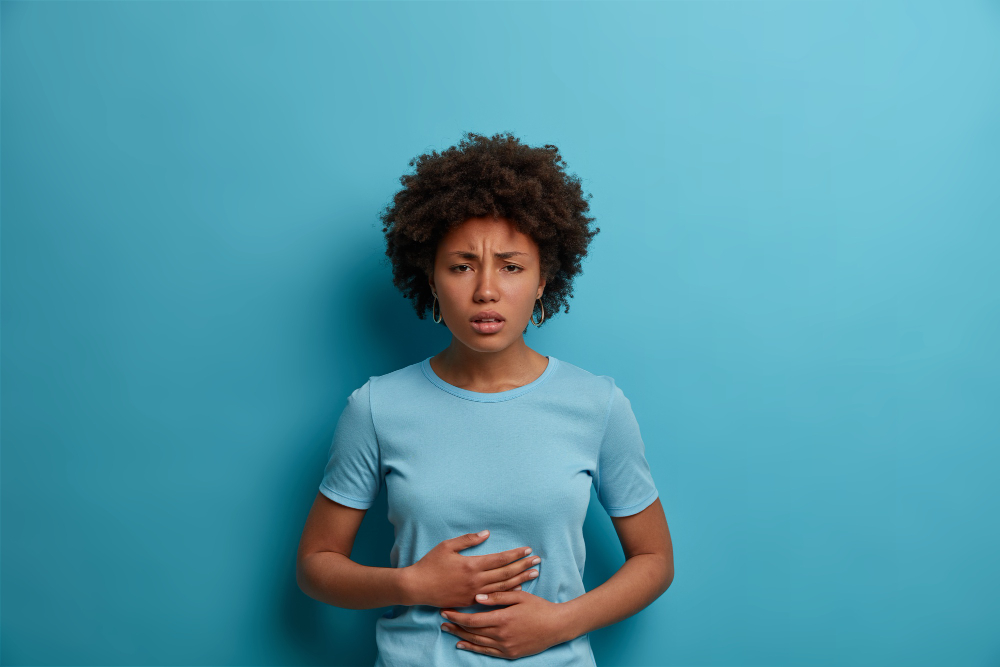 An Afro woman experiences discomfort in her stomach, placing her palms gently on her abdomen.