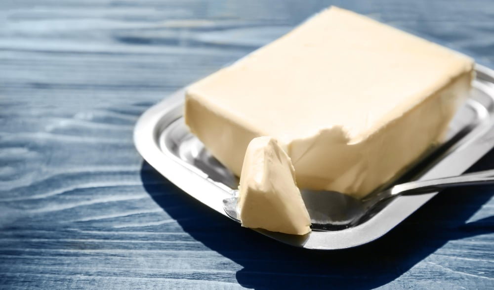 Dish with butter and shovel on wooden table closeup