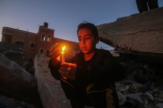 Palestinian children hold candles near buildings destroyed in Israeli air strikes in the southern Gaza Strip city of Rafah, on May 25, 2021