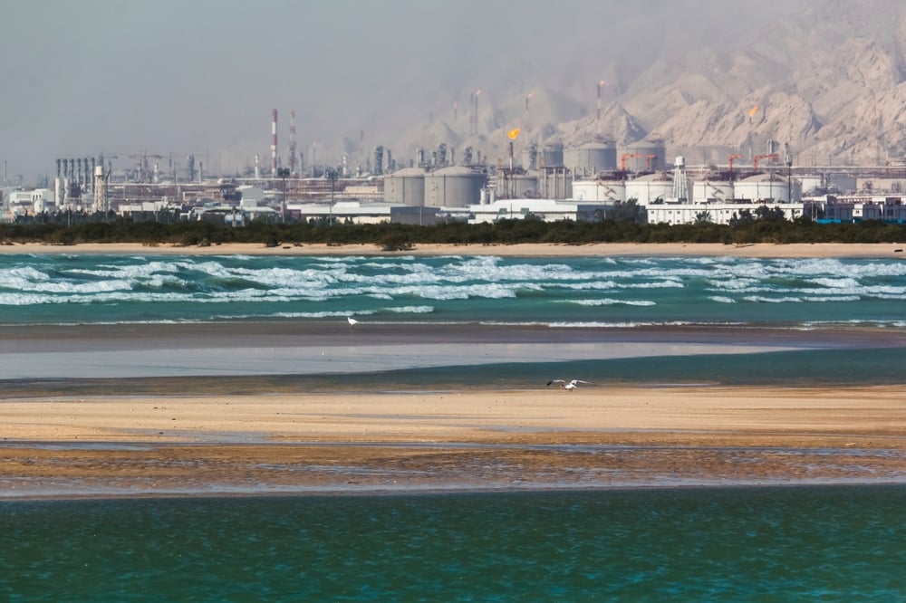 Seascape of blue waves and flying birds with a background of a refinery complex in southern province of Bushehr, Iran