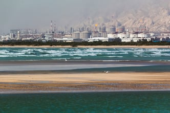 Seascape of blue waves and flying birds with a background of a refinery complex in southern province of Bushehr, Iran