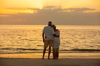 Senior man and woman couple embracing at sunset or sunrise on a deserted tropical beach