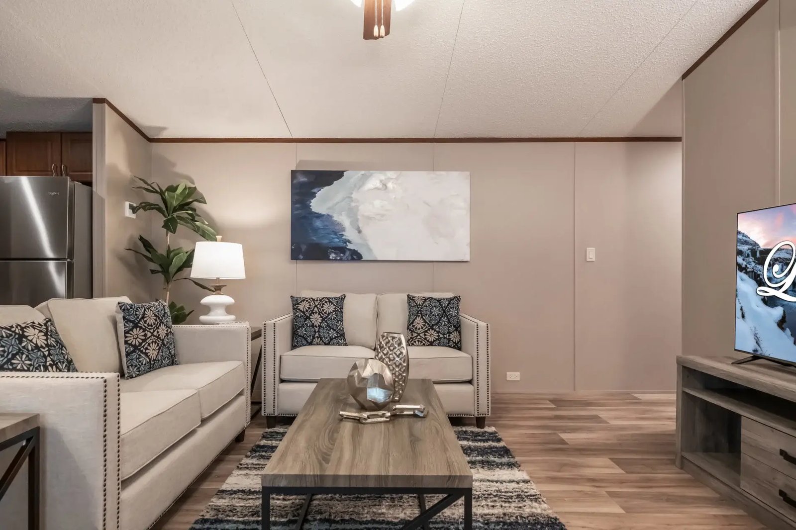 Front view of the living room in The Lisa with coordinated seating, coffee table, television console, and open access to the kitchen