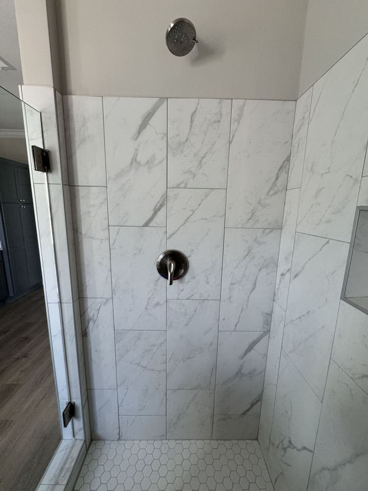 Marble-look tile shower with hexagon floor in The Lilly II 5075-76-4-44 by Franklin Homes