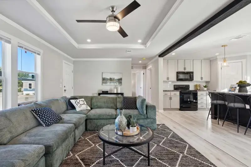 Bright living room with sectional seating and adjoining kitchen in The Carol by Champion Homes
