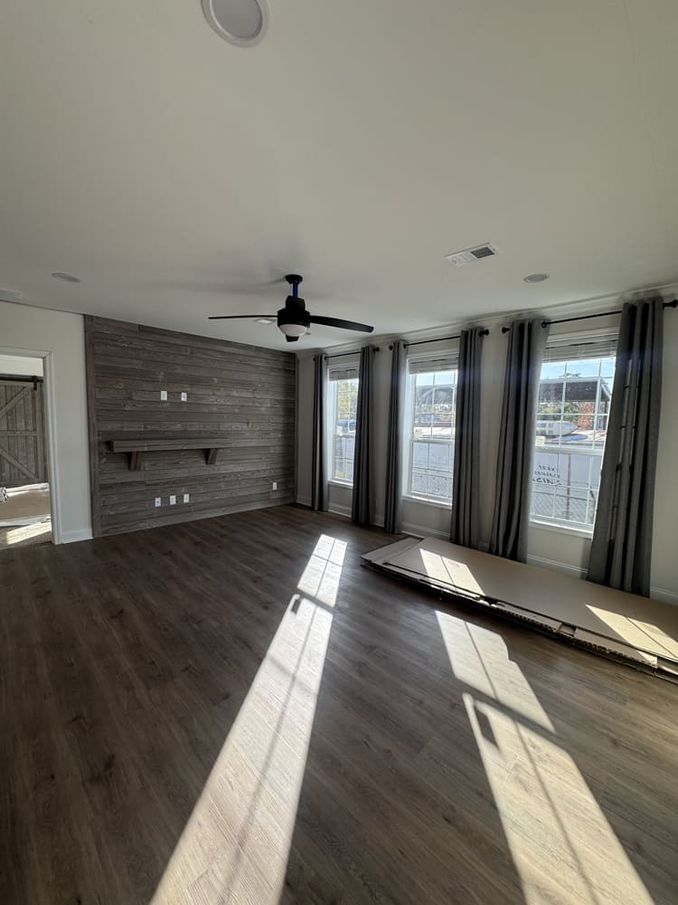 Spacious living room with shiplap accent wall, large windows and ceiling fan in The Shoreline manufactured home