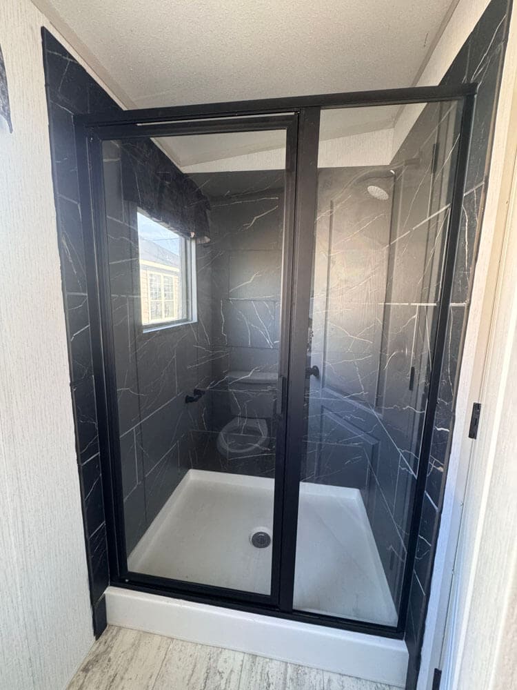 Glass walk-in shower with dark marble-look walls in The Lucia